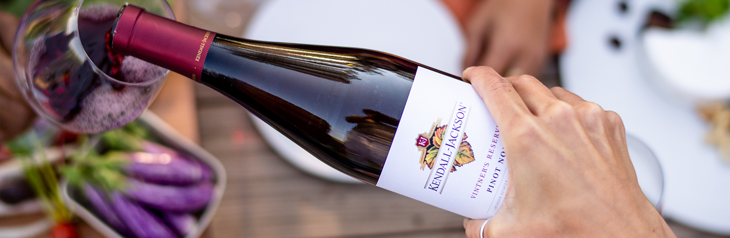 Close up of a hand pouring Kendall-Jackson Vintner's Reserve Pinot Noir into a glass from above.